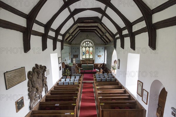 Raised angle view looking east down the nave towards the altar and east window with wooden pews, simple wood roof beams, whitewashed walls, interior of village parish church at Friston, Suffolk, England, UK. Mounted on the wall is a large Stuart Royal Coat of Arms of King James 1st 1605