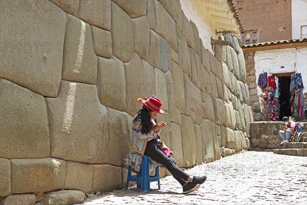 Peruvian woman with hat sitting in front of the traditional Inca wall in Calle Hatunrumiyoc, old town, Cusco, Cusco province, Peru, South America