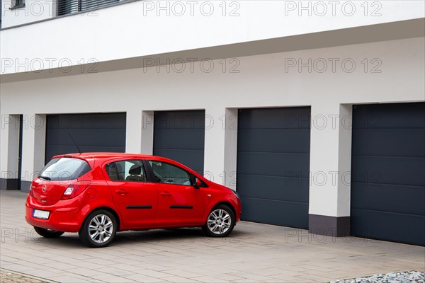 An Opel Corsa is parked in front of one of several garages with black sectional doors