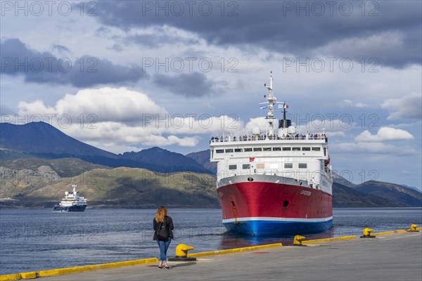 A woman watches a cruise ship named Expedition depart from the harbour of the Beagle Channel, Ushuaia, Tierra del Fuego Island, Patagonia, Argentina, South America