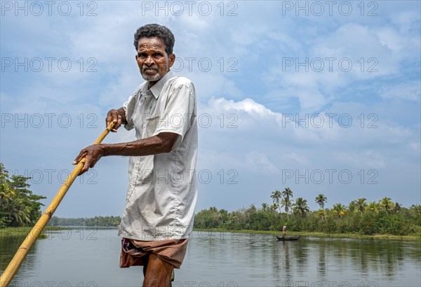 A man navigates a boat through the canals of the Kerala Backwaters using a long pole, Vembanad Lake, Kerala, India, Asia