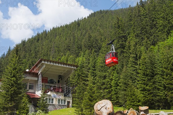 Cable car station in a green mountain landscape with a red cable car gondola surrounded by fir trees and a pile of wood, Balea Cascada cable car station, Transfogarasan High Road, Transfagarasan, TransfagaraÈ™an, FagaraÈ™ Mountains, Fagaras, Transylvania, Transylvania, Transylvania, Ardeal, Transylvania, Carpathians, Romania, Europe