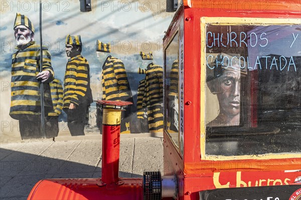 Red trolley for selling churros, behind a graffito with men in convict clothing, Ushuaia, Tierra del Fuego Island, Patagonia, Argentina, South America