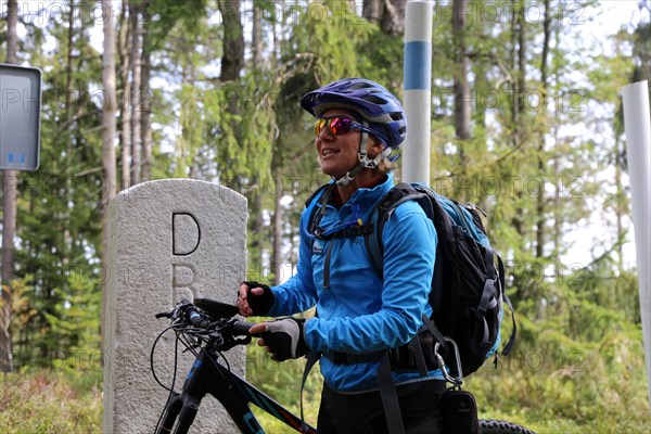 Mountain bike tour through the Bavarian Forest with the DAV Summit Club: Tour guide Birgit Aschenbrenner at a boundary stone marking the border between Germany (Bavarian Forest) and the Czech Republic (Bohemian Forest)