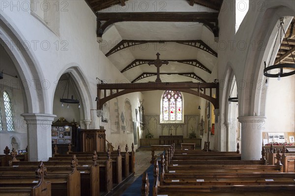 Looking east down the nave towards the altar and east window with historic wooden pews, roof beams, whitewashed walls with columns, interior of village parish church at Hintlesham, Suffolk, England, UK