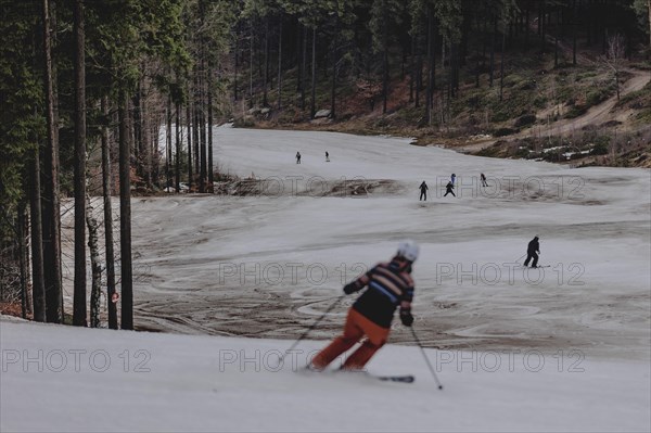 Skiers skiing on an artificially snow-covered and dirty slope, taken on a ski slope in the Jizera Mountains ski area near Albrechtice v Jizerskych Horach, 05.02.2024. The Czech low mountain range with its ski area is affected by increasingly warmer and shorter winters