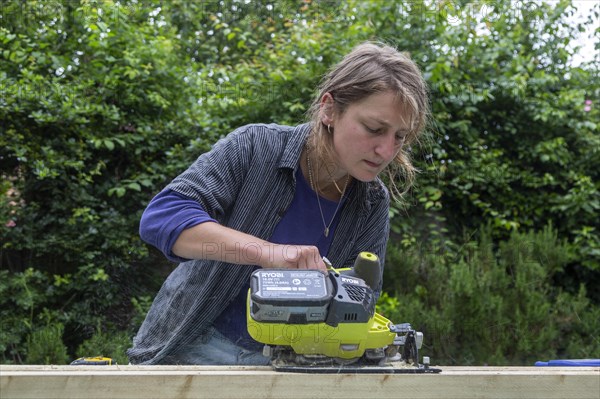Young woman using electric power sawing tool without safety googles or protective clothing, model released