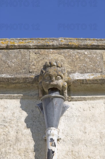 Gargoyle grotesque face drainpipe on wall medieval church of Saint John, Inglesham, Wiltshire, England, UK