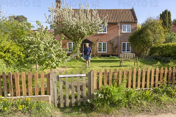 Woman watering garden with hosepipe in front of red brick historic detached house, Shottisham, Suffolk, England, UK