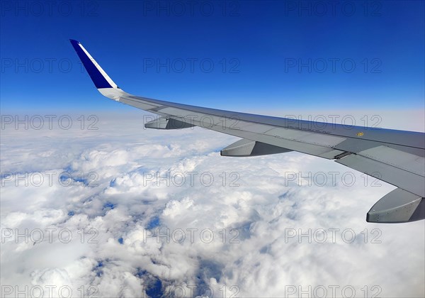 View from the aircraft while flying on a wing above the clouds with a blue sky