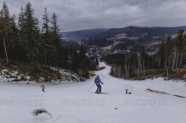 Skiers skiing on an artificially snow-covered and dirty slope, taken on a ski slope in the Jizera Mountains ski area near Albrechtice v Jizerskych Horach, 05.02.2024. The Czech low mountain range with its ski area is affected by increasingly warmer and shorter winters