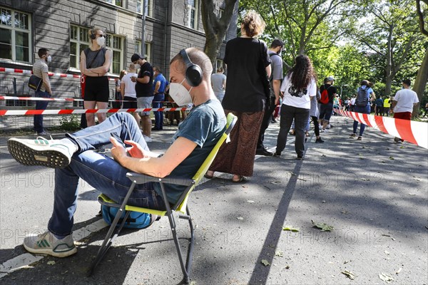 A vaccinated person sits on his folding chair in a long queue. Neighbourhood residents in the Tempelhof Schoeneberg district can get vaccinated free of charge and without registering here, Berlin, 05.06.2021