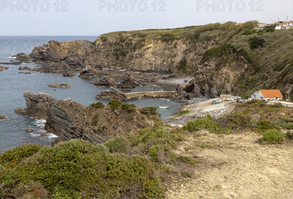 Rocky rugged coastline near fishing port village of Azenha do Mar, Alentejo Littoral, Portugal, southern Europe, small fishing boat arriving back in the harbour, Europe