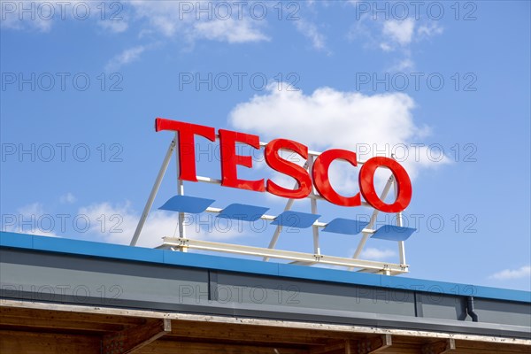 Bright red Tesco store sign against blue sky and white fluffy cumulus clouds