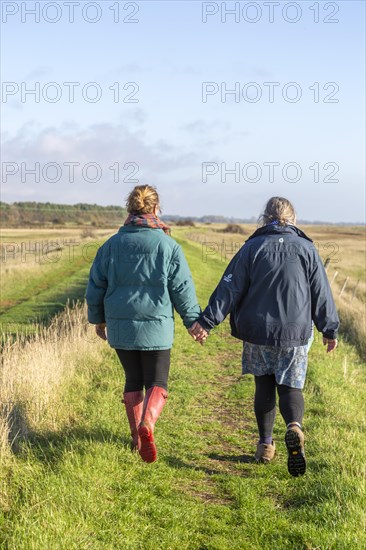 Mother and adult daughter walking together by the River Ore, Suffolk, England, UK from behind holding hands