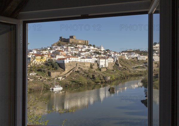Historic hilltop walled medieval village of Mertola with castle, on the banks of the river Rio Guadiana, Baixo Alentejo, Portugal, Southern Europe framed by hotel window, Europe