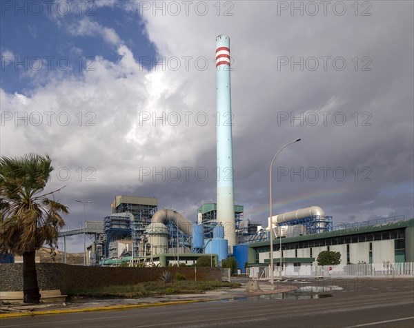 Rainbow in stormy sky behind tall blue industrial cement factory chimney, Carboneras, Almeria, Spain, Europe