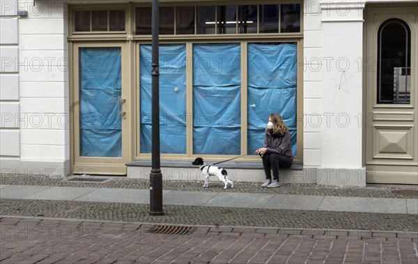 A woman sits with her dog in front of a closed shop. Customers who want to buy in retail stores in the city must present a negative corona test, Potsdam, 27.03.2021