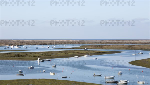 Coastal landscape of salt marsh with boats moored in meandering river drainage channels along the coastline off Faro, Algarve, Portugal, Europe