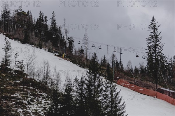 A chairlift stands out between individual trees in a thinned-out forest area, taken on a ski slope in the Jizera Mountains ski area near Albrechtice v Jizerskych Horach, 05.02.2024. The Czech low mountain range with its ski area is affected by increasingly warmer and shorter winters