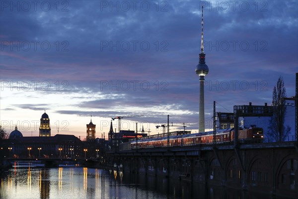 City view Berlin in the evening. View across the Spree to the television tower and the red town hall, a Deutsche Bahn regional train at the S-Bahn station at Janowitzbruecke, 29/03/2021