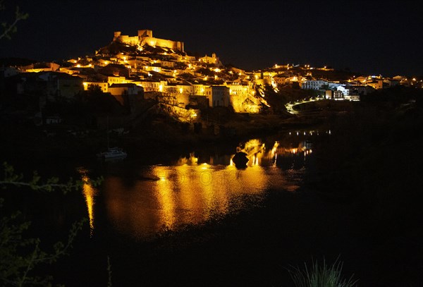 Historic hilltop walled medieval village of Mertola with castle, on the banks of the river Rio Guadiana, Baixo Alentejo, Portugal, Southern Europe nighttime with illumination of orange street lights, Europe