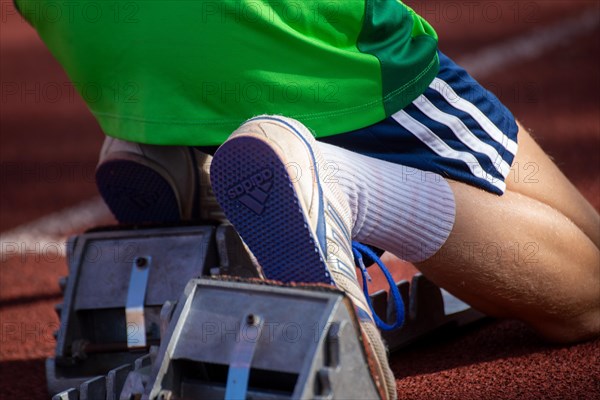 Young track and field athlete with Adidas spikes at the starting block in front of a sprint