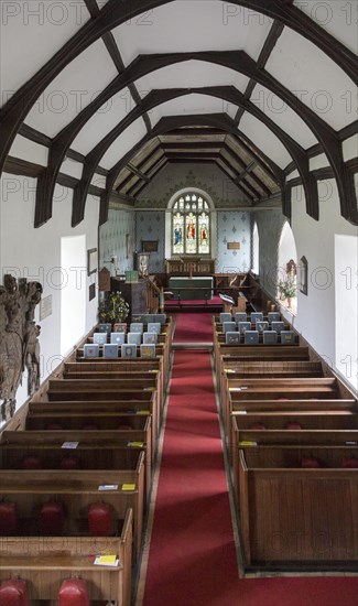 Raised angle view looking east down the nave towards the altar and east window with wooden pews, simple wood roof beams, whitewashed walls, interior of village parish church at Friston, Suffolk, England, UK. Mounted on the wall is a large Stuart Royal Coat of Arms of King James 1st 1605