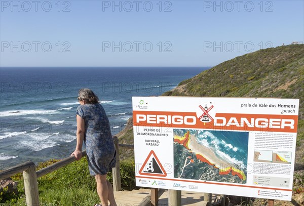 Woman looking to sea by danger notice, Praia de Vale do Homens beach, Rogil, Algarve, Portugal, Europe