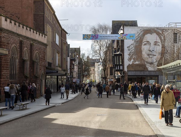 Shoppers in pedestrianised High Street, Exeter city centre, Devon, England, UK mural of woman by Vhils, artist Alexandre Manuel Dias