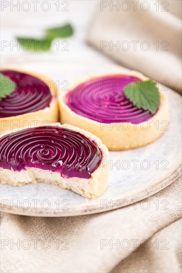 Sweet tartlets with jelly and milk cream with cup of coffee on a white wooden background and linen textile. Side view, close up, selective focus