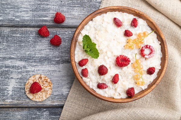 Rice flakes porridge with milk and strawberry in wooden bowl on gray wooden background and linen textile. Top view, flat lay, close up