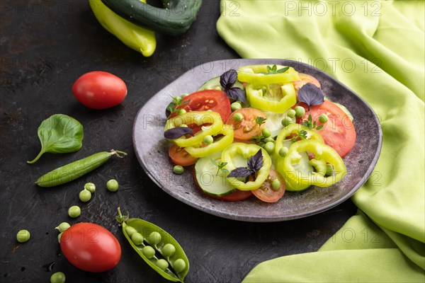 Vegetarian salad from green pea, tomatoes, pepper and basil on a black concrete background and green textile. Side view, close up