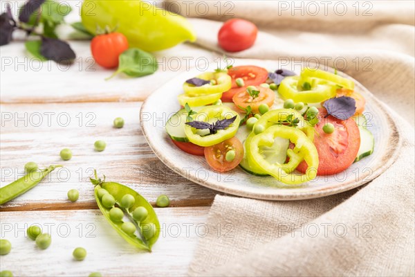 Vegetarian salad from green pea, tomatoes, pepper and basil on white wooden background and linen textile. Side view, close up, selective focus