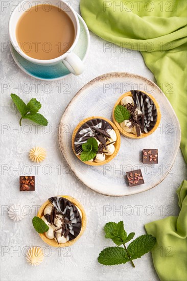 Sweet tartlets with chocolate and cheese cream with cup of coffee on a gray concrete background and green textile. top view, flat lay, close up