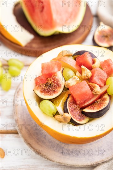 Vegetarian fruit salad of watermelon, grapes, figs, pear, orange, cashew on white wooden background and linen textile. Side view, close up, selective focus