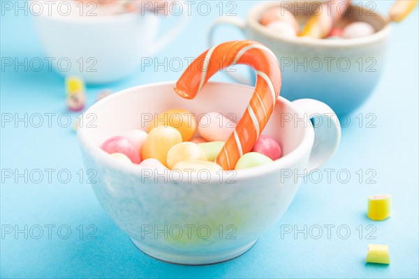 Heap of multicolored caramel candies in cups on blue pastel background. close up, side view, selective focus