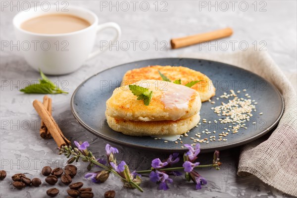 Cheese pancakes on a blue ceramic plate and a cup of coffee on a gray concrete background. side view, close up