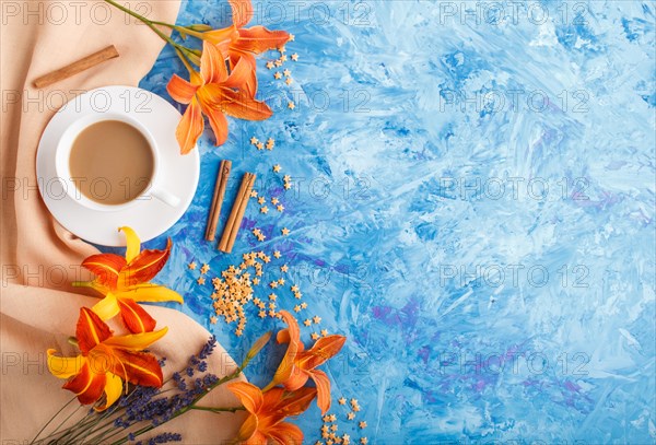 Orange day-lily and lavender flowers and a cup of coffee on a blue concrete background, with orange textile. Morninig, spring, fashion composition. Flat lay, top view, copy space