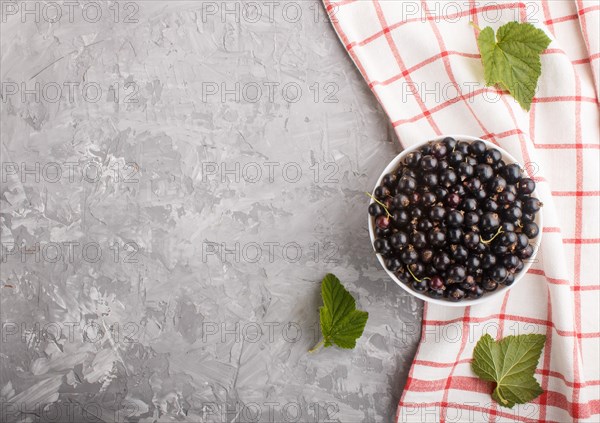Fresh black currant in white bowl and linen textile on gray concrete background. top view, copy space