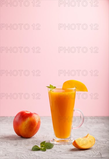 Glass of peach juice on a gray and pink background. Morninig, spring, healthy drink concept. Side view, copy space