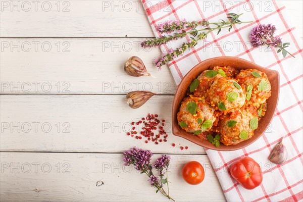 Pork meatballs with tomato sauce, oregano leaves, spices and herbs in clay bowl on a white wooden background with linen textile. top view, flat lay, copy space
