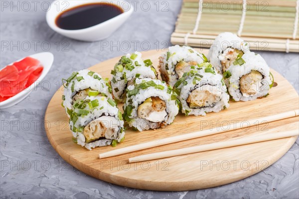 Japanese maki sushi rolls with green onion, chopsticks, soy sauce and marinated ginger on wooden board on a gray concrete background. Side view, close up, selective focus