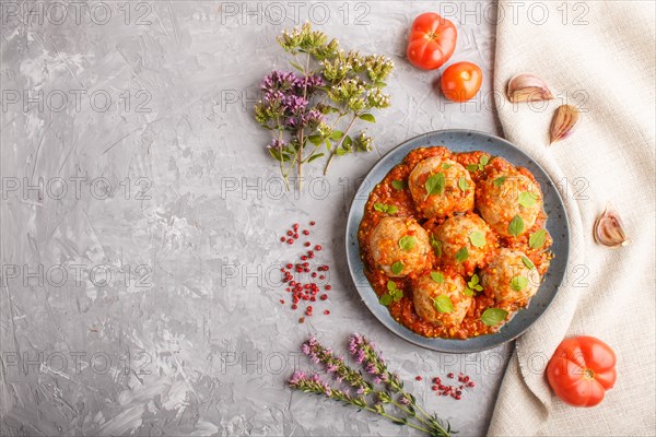 Pork meatballs with tomato sauce, oregano leaves, spices and herbs on blue ceramic plate on a gray concrete background with linen textile. top view, flat lay, copy space