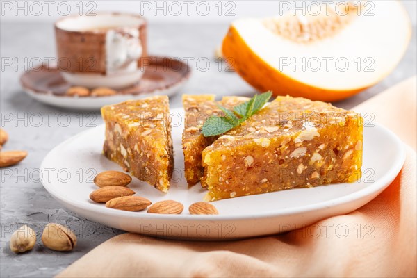 Traditional turkish candy cezerye made from caramelised melon, roasted walnuts, hazelnuts, cashew, pistachios on white ceramic plate and a cup of coffee on a gray concrete background. side view, close up, selective focus