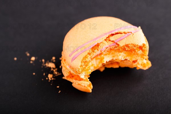 Bitten orange macaron or macaroon cake on black background. side view, close up, macro, selective focus
