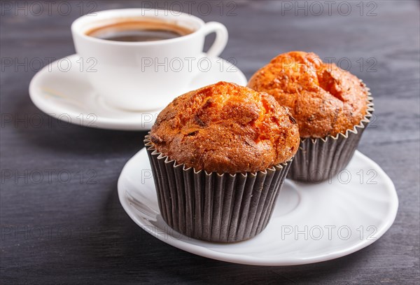 Two carrot muffins with cup of coffee on white plate on black wooden background. closeup