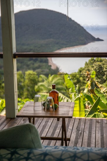 Rum limes and glasses on a table of a terrace in the foreground, in the background the beach Grande Anse on Basse Terre, Guadeloupe, the French Antilles and the Caribbean, North America