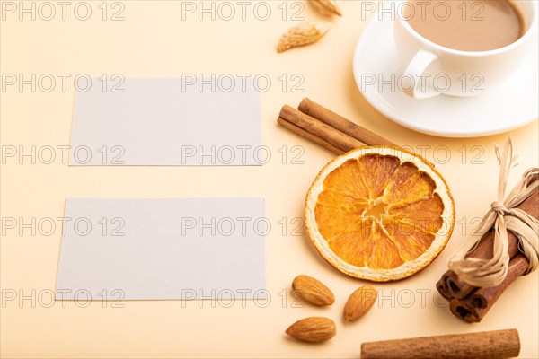 Composition of gray paper business cards, almonds, cinnamon and cup of coffee. mockup on orange background. Blank, side view, still life, copy space