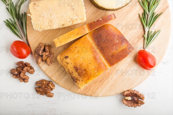 Smoked cheese and various types of cheese with rosemary and tomatoes on wooden board on a white wooden background. Top view, flat lay, close up
